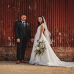 Bride and groom pose by rustic red wall.