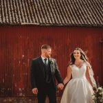 Bride and groom holding hands, red barn background.