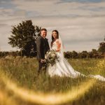 Wedding couple standing in field with flowers.