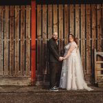 Bride and groom holding hands by wooden fence.