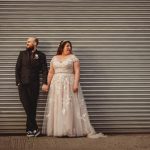 Wedding couple holding hands by a shuttered wall.