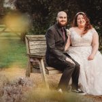 Couple in wedding attire sitting on a bench.