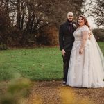 Couple in wedding attire on lawn in autumn.