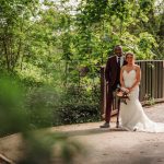 Happy couple in wedding attire on a woodland path.