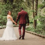 Newlyweds walking hand-in-hand in forest path.