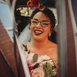 Smiling bride with glasses holding bouquet in car