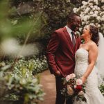 Bride and groom smiling in garden setting.