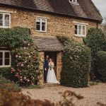 Bride and groom outside rustic ivy-covered cottage.