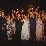 Wedding guests holding sparklers at night celebration.