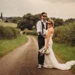 Bride and groom pose on countryside road.