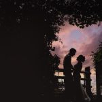 Silhouette couple under sunset sky by trees.