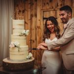 Couple cutting tall wedding cake with flowers.