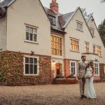 Couple posing outside a large, ivy-covered house.