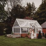 Couple beside white greenhouse in garden setting.