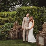 Wedding couple posing with lion statues in garden.