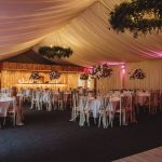 Elegant wedding reception with floral centrepieces and draped ceiling.