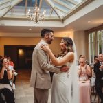 Bride and groom first dance with guests clapping.