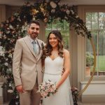 Bride and groom with floral arch indoors.