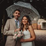 Smiling couple under lace umbrella at wedding.