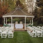 Outdoor wedding venue with decorated white chairs and gazebo.