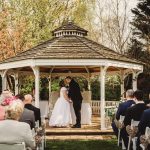 Outdoor wedding ceremony under gazebo with guests seated.