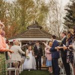 Bride and groom leaving gazebo, guests celebrate.