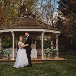 Wedding couple embracing by a garden gazebo.