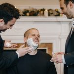 Groom surrounded by friends during wedding shaving ritual.