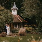 Couple poses by garden cottage.