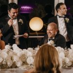 Wedding party laughing at speech with floral decorations.