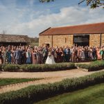 Large wedding group photo outside rustic barn.