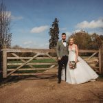 Bride and groom standing by a wooden gate outdoors.