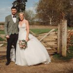 Bride and groom posing by rustic wooden gate.