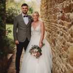 Bride and groom smiling by stone wall.