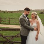 Bride and groom embracing by rural fence