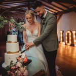 Couple cutting wedding cake with LOVE sign background.