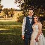 Couple smiling on wedding day in sunny garden.