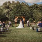 Outdoor wedding ceremony under wooden arch.