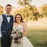 Smiling couple in a field holding flowers.