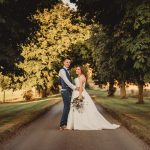 Bride and groom on tree-lined country lane.