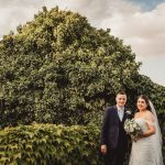 Bride and groom standing in front of lush greenery.