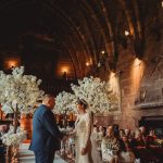 Indoor wedding ceremony with guests and floral decor.