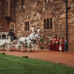 Horse-drawn wedding carriage passes bridesmaids in red dresses.