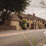 Charming Cotswolds stone cottage beside country road.