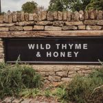 Rustic sign: Wild Thyme & Honey, stone wall background.