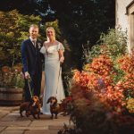 Couple with dachshunds in garden on wedding day.