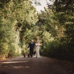 Bride and groom walking with dogs in forest.