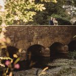 Couple standing on historic stone bridge in sunlight.