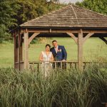 Couple in gazebo amid lush green landscape.