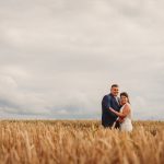 Couple embracing in wheat field under cloudy sky.